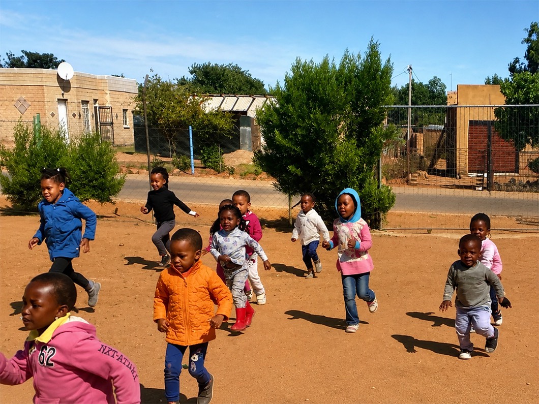 Zonke Izizwe children running across the yard, with the houses of Mandela Village behind them