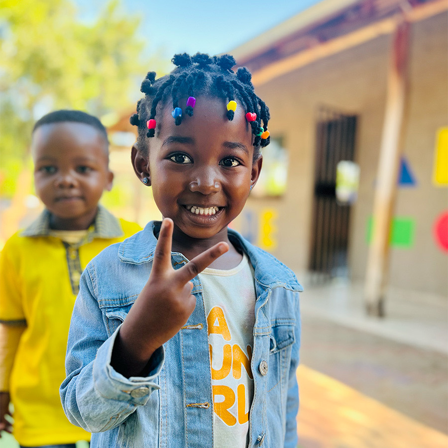 A Zonke Izizwe pupil smiling and making a peace sign outside the school