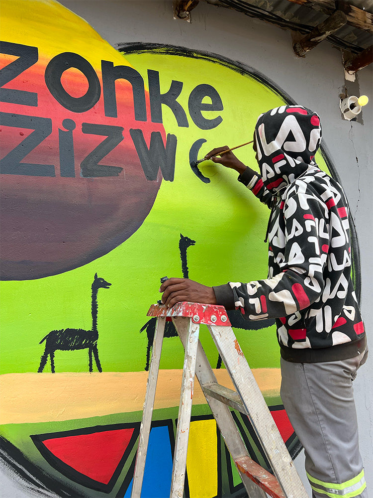 A painter on a stepladder finishing the Zonke Izizwe mural on the school wall