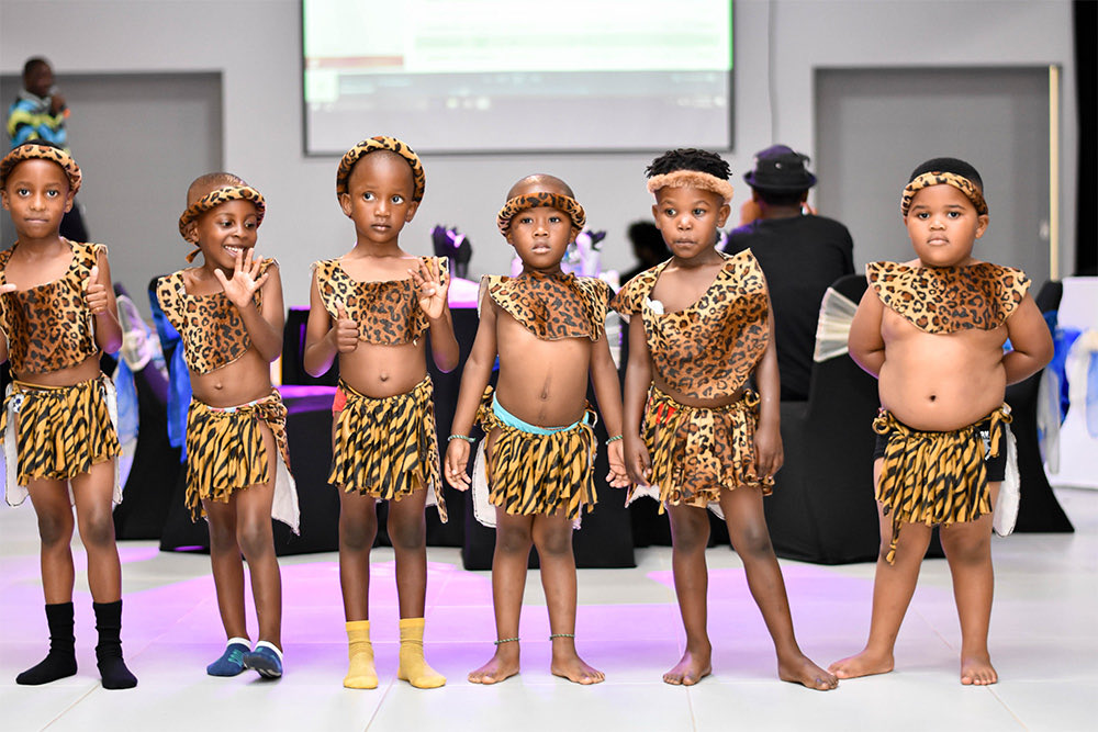 Six children in leopard-print traditional dress standing on stage
