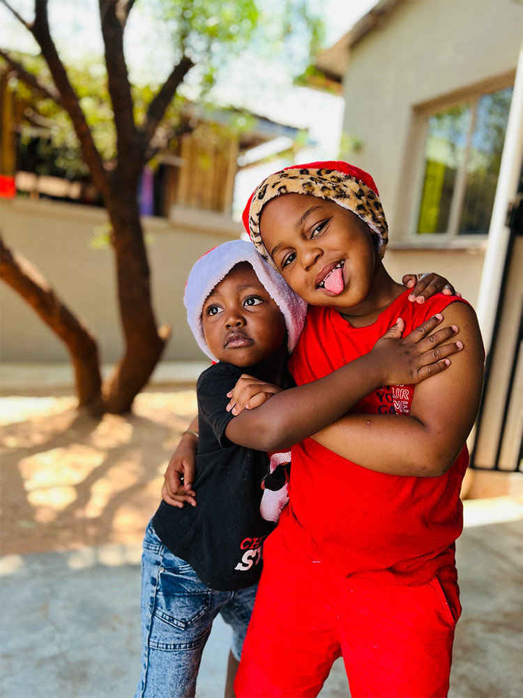 Two children in festive hats hugging outside the school