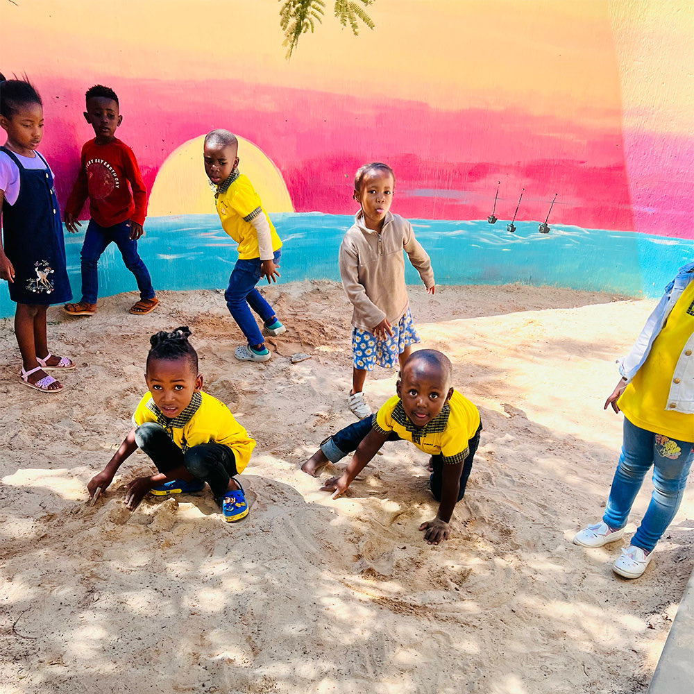 Children playing in the sand pit in front of a painted sunset mural