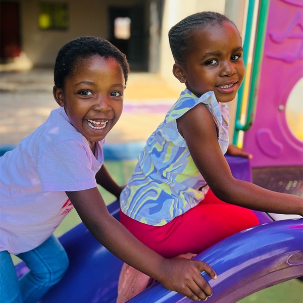 Two Zonke Izizwe pupils laughing together on the playground climbing frame